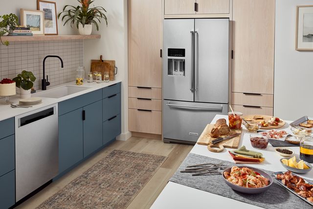 Front view of a modern kitchen with a stainless steel counter depth refrigerator fit into light wooden cabinetry