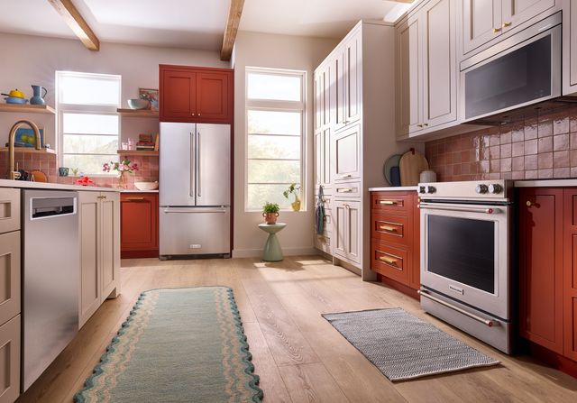Front view of a modern kitchen with orange cabinetry and stainless steel KitchenAid appliances including a dishwasher, french door refrigerator, range, and over the range mircowave.
