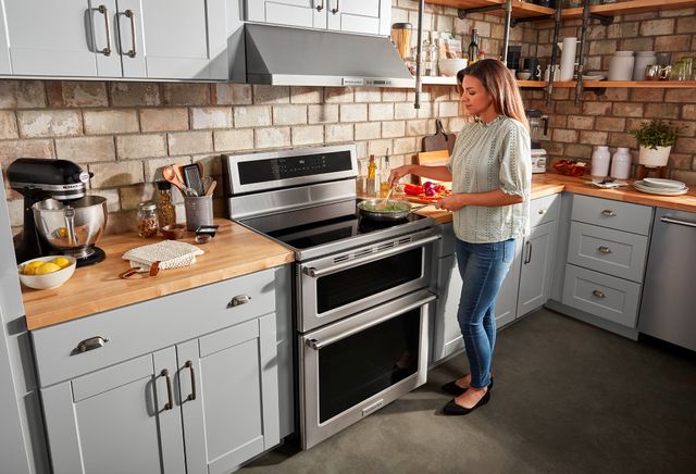 front view of a woman cooking on a freestanding range in a modern rustic kitchen with various kitchenaid appliances