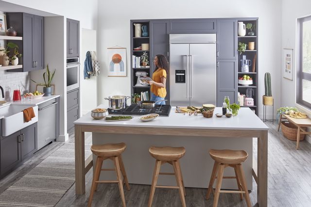 Front view of a modern kitchen with a woman cooking on a KitchenAid cooktop