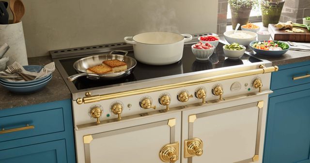 standing view of a white la cornue induction range with a pan cooking and various dishes on top