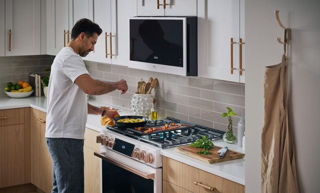 side view of a man cooking on a white gas range in a modern kitchen