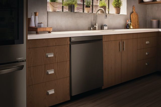 Front view of a dimly lit kitchen with a black stainless steel LG dishwasher