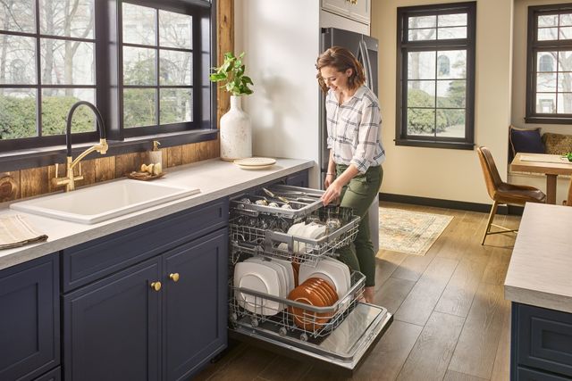 Front view of a woman leaning over and loading an LG dishwasher in a modern kitchen on a foggy morning