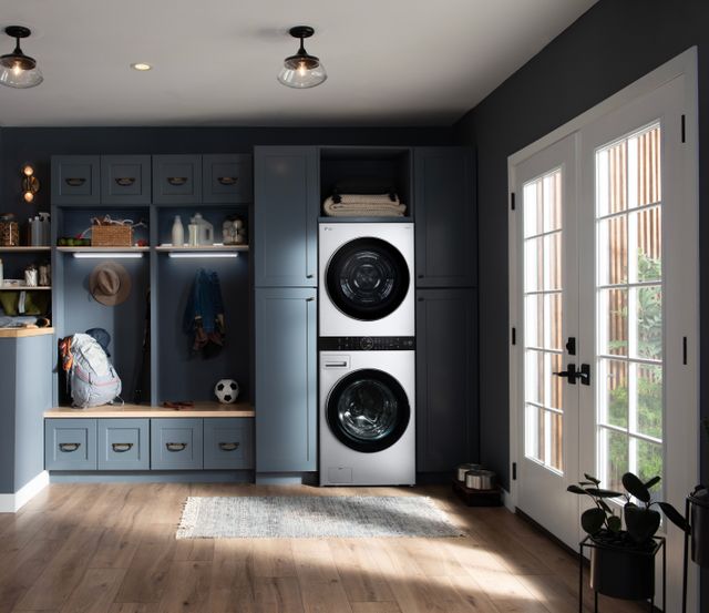 Front view of a white LG WashTower in a modern mud room with blue cabinetry and white walls.