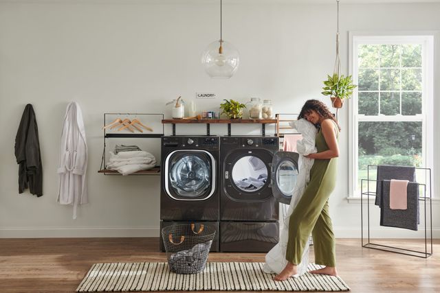 front view of a woman holding a white comforter and smiling in front of an LG washer and dryer