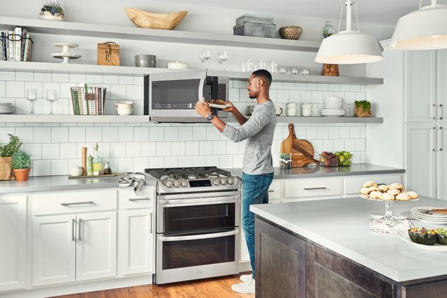 front view of a man opening his microwave in a modern kitchen