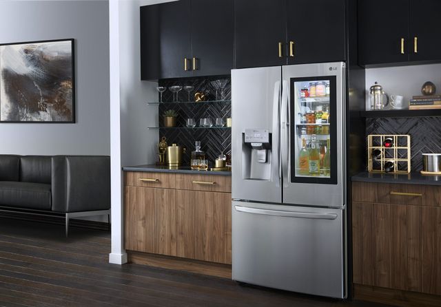 front view of a modern kitchen with an LG instaview french door refrigerator in front of a sleek black tile backsplash decorated with various glass and gold drinkware