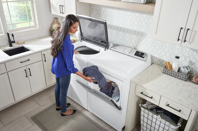 View of a woman loading a Maytag dryer in a modern laundry room.