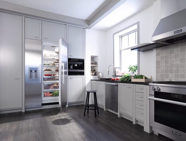 front view of a modern kitchen with white cabinets and stainless steel appliances including a side by side refrigerator, built in coffee machine, dishwasher, and range oven