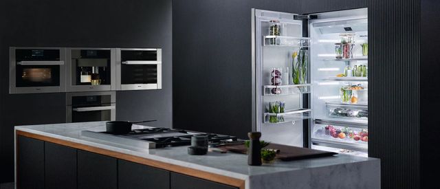 front view of a black contemporary kitchen with grey counters and miele appliances. in the foreground is a black kitchen island with white cabinetry and various black cookware on top