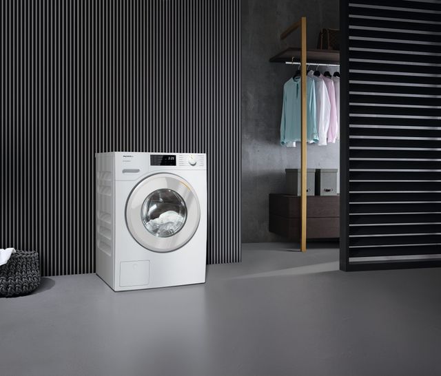Front view of a Miele washing machine next to a closet full of clothes 