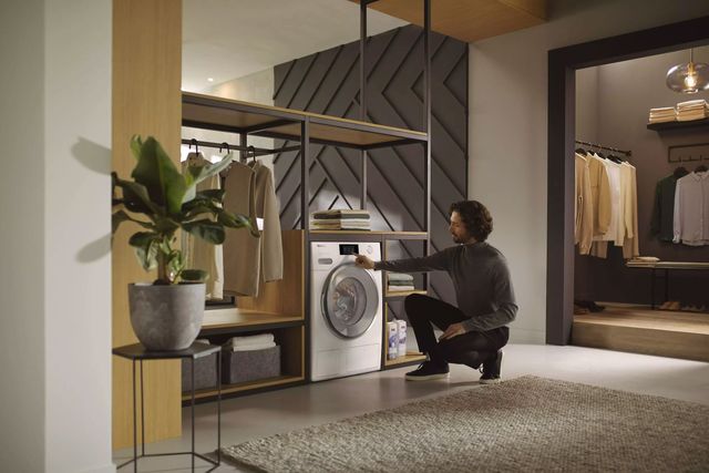 Front view of a modern home with a Miele ventless dryer and a man kneeling down to look inside