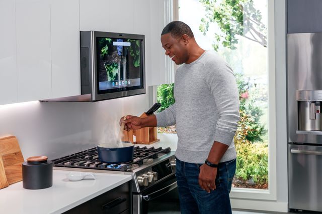 view of a man stirring a pot on a ge profile range, and over the range is a microwave with a smart screen lit up