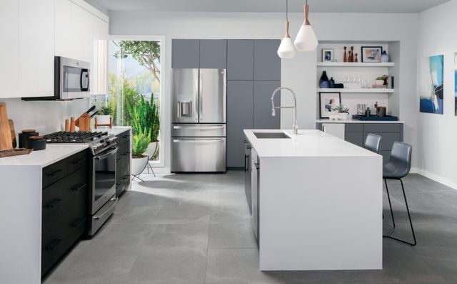 front view of a modern kitchen with white and grey cabinetry. and a ge profile french door refrigerator centered in the wall of cabinets