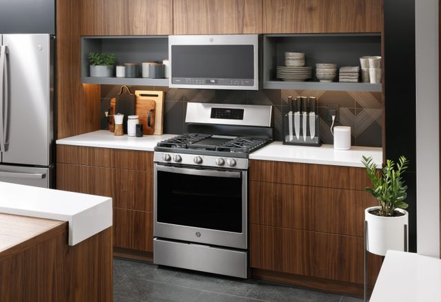 front view of a contemporary kitchen with grey floors and walls and brown wooden cabinetry, with a GE Profile range and over the range microwave
