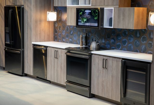 view of a modern kitchen with wooden cabinets and black ge profile appliances, inluding a range, over the range microwave, wine cooler, and a refrigerator
