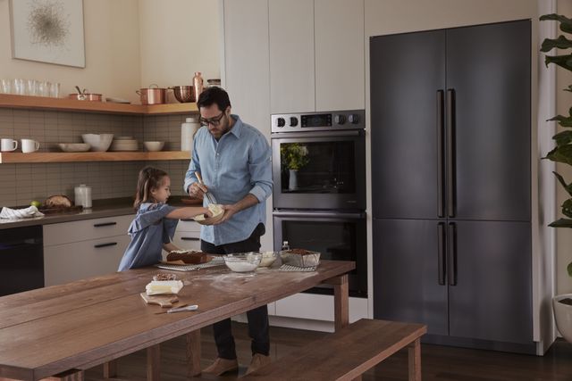 front view of a man and his chilc baking banana bread in their kitchen with a large stainless steel LG refrigerator behind them