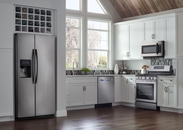 front view of a modern kitchen with white cabinets and walls, with various stainless steel appliances from left to right, a side by side refrigerators, dishwasher, range, and over the range microwave