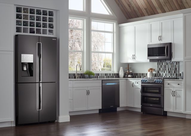 Front view of a modern kitchen with a black and stainless steel refrigerator and matching appliances.