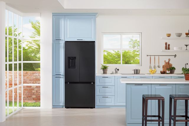 front view of a black stainless steel french door refrigerator in a bright kitchen with light blue cabinets and white walls