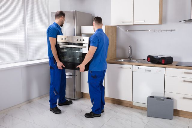 front view of two men installing a wall oven in a modern kitchen