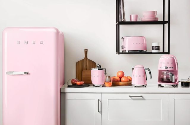 front view of a light pink Smeg fridge with matching Smeg small appliances next to it