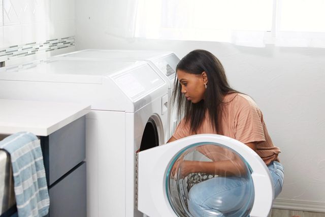 view of a woman crouching down and reaching into a Speed Queen front load washer