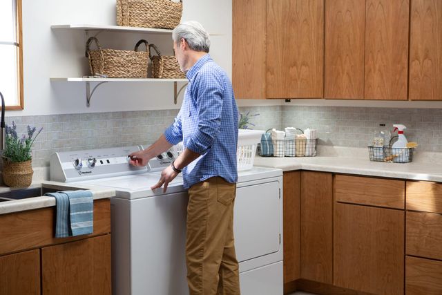 View of a man turning the knob on a speed queen washer, with a dryer next to it in a modern laundry room