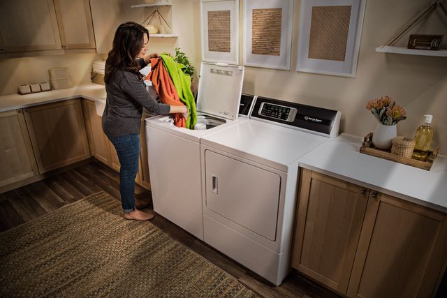 front view of a woman loading a speed queen washer in a casual laundry room