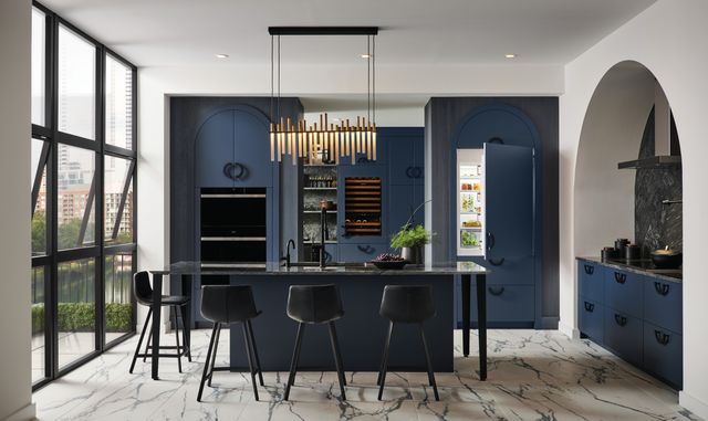 Front view of a modern kitchen with a slightly opened panel ready refrigerator matching the blue cabinetry