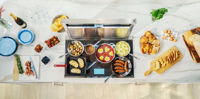 Top view of a Thermador cooktop with various foods cooking on top and displayed across the countertop