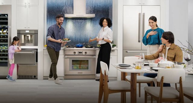 Front view of a family having dinner in a modern kitchen with a 30 inch gas range and other various Thermador appliances