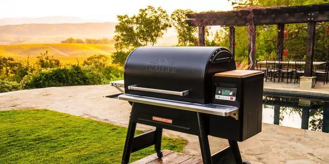 front view of a traeger grill in front of a pool and outdoor patio area with a large field in the background