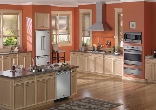 Front view of a modern kitchen with orange walls and stainless steel Viking appliances including a wall oven and microwave.