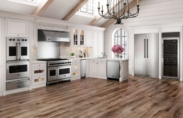front view of a modern kitchen with white cabinets, two wall ovens, an induction range, trash compactor, dishwasher, and refrigerator