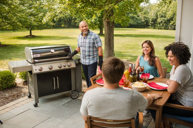 Front view of a family sitting outside and grilling with a Weber freestanding grill