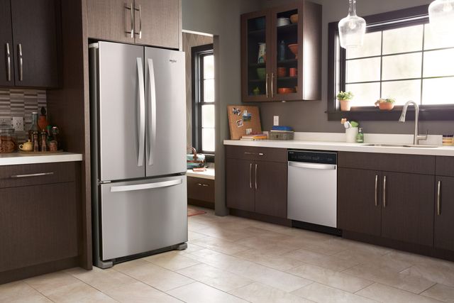 Front view of a casual kitchen with brown cabinetry and a Whirlpool stainless steel refrigerator.