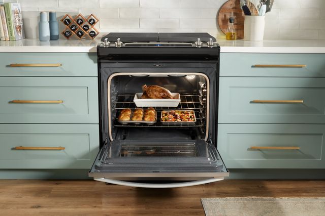 front view of an opened whirlpool gas range built into light blue cabinetry with white countertops and backsplash