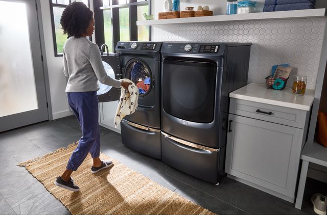 Front view of a woman adding an article of clothing to her running Whirlpool front load washer in a modern laundry room