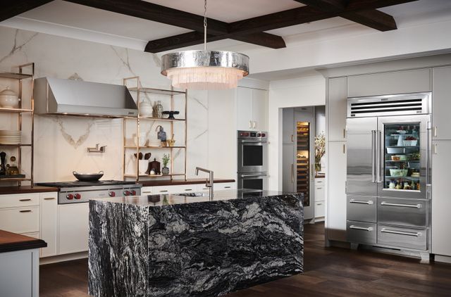 Front view of a luxury kitchen with a marble island, white walls and cabinetry, and luxury kitchen appliances and upgrades.