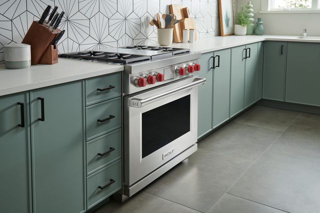 front left view of a wolf gas range built into green cabinety in a modern kitchen with white countertops