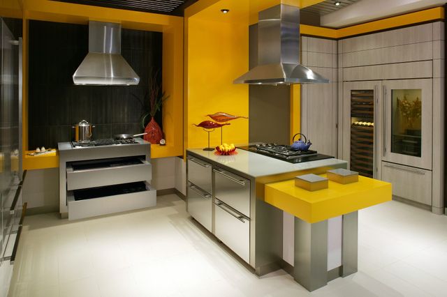 Front view of a large modern kitchen with yellow walls and two stainless steel range hoods