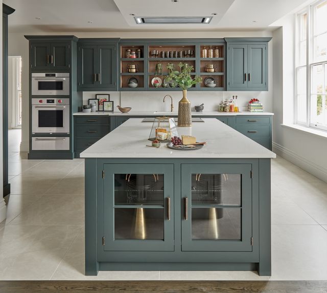 Front view of a modern kitchen with an island, white walls, blue cabinetry, and a Wolf M series wall oven