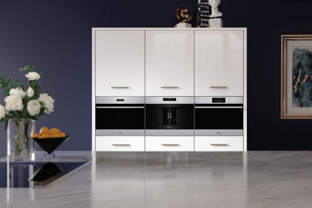 Front view of a modern kitchen over an island looking at three built in Wolf wall ovens