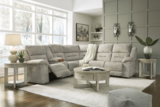 front view of a beige reclining l-shaped sectional in a casual living room with grey wooden tables and walls