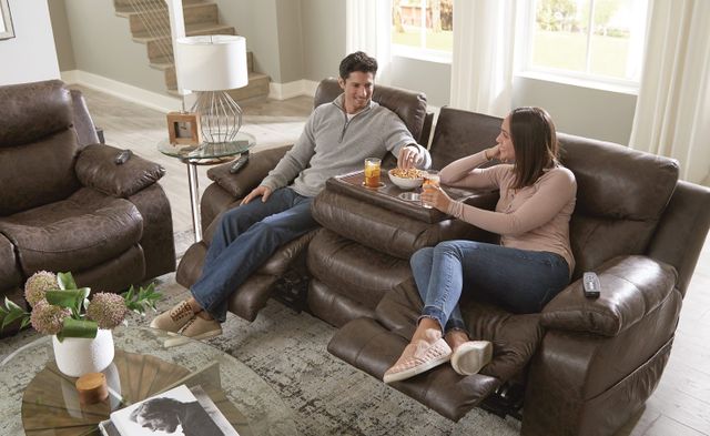front view of two people sitting on a power reclining sofa with a storage console and cupholders