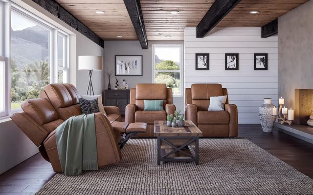 front view of a modern living room with white walls and a large window on the left wall. On the left is a Flexsteel recliner sofa, with a coffee table in front of it, facing the camera are two matching flexsteel brown leather recliners