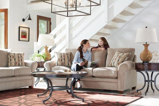 view of a modern living room with a La-Z-Boy sofa and chair, with a woman sitting on the sofa reading and a child leaning over talking to her