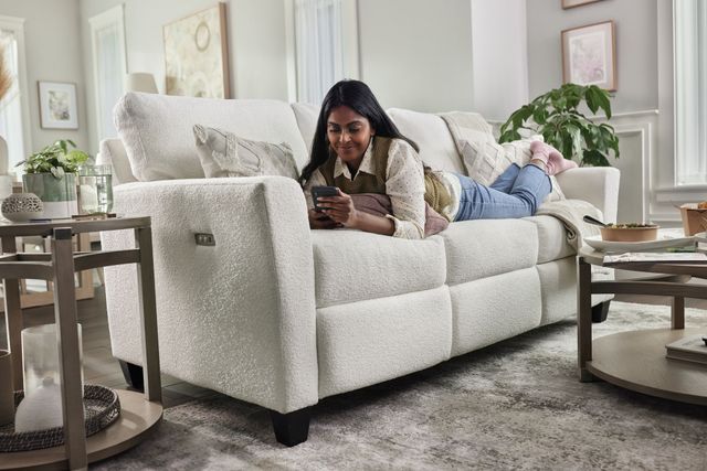 Low view of a woman laying on her stomach on her phone on a fluffy white La-Z-Boy sofa